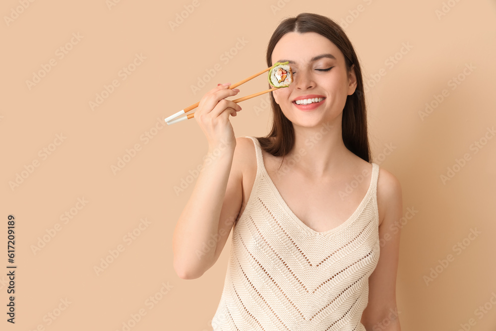 Young woman with sushi roll on beige background