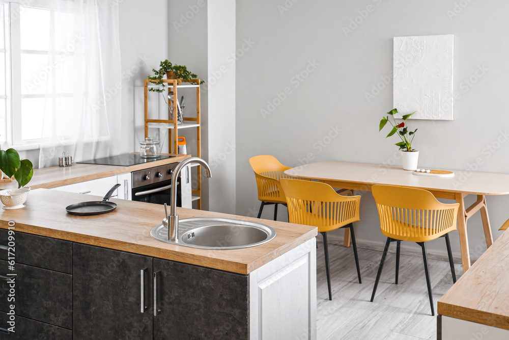 Interior of light kitchen with dining table and sink on wooden countertop