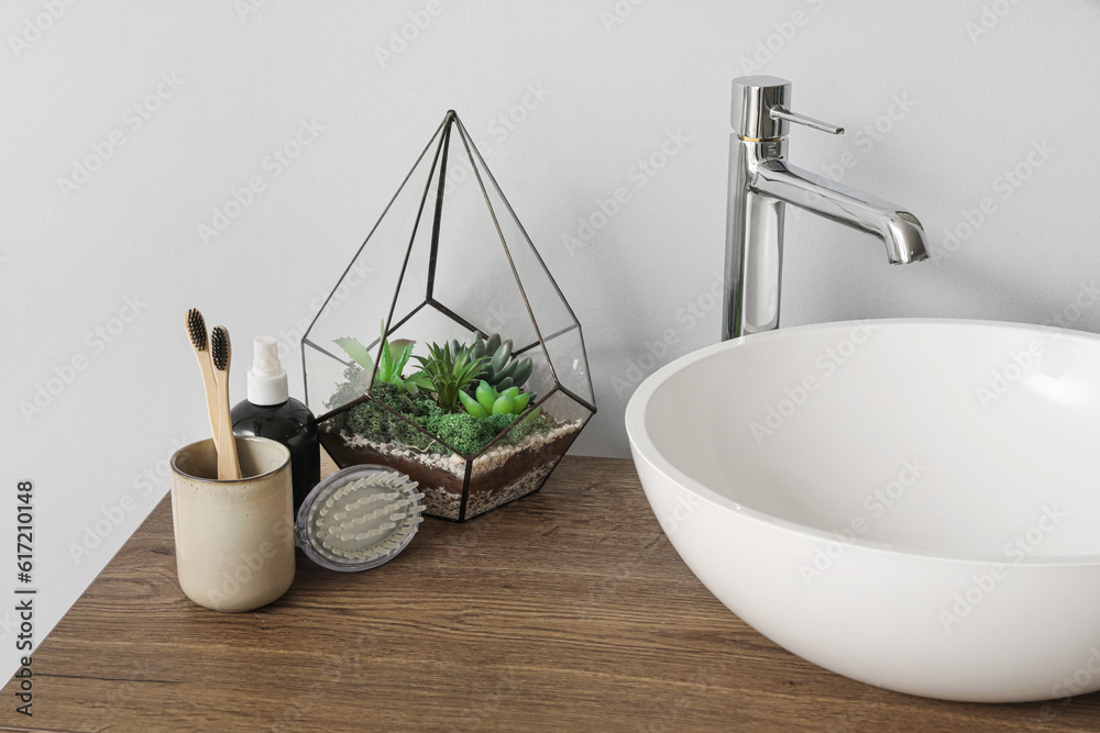 Table with sink bowl, toothbrushes and florarium in bathroom