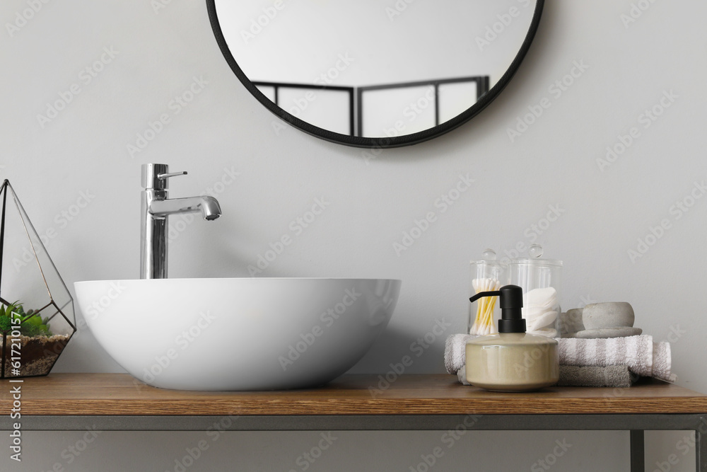 Table with sink bowl, soap dispenser and bath accessories in bathroom