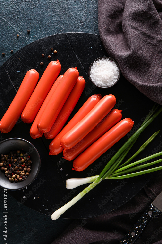 Board with tasty thin sausages and green onion on dark background