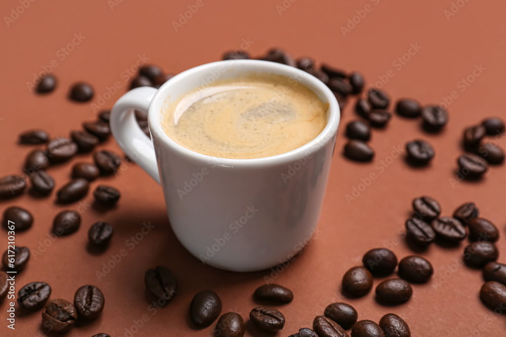 Cup of hot espresso and coffee beans on brown background