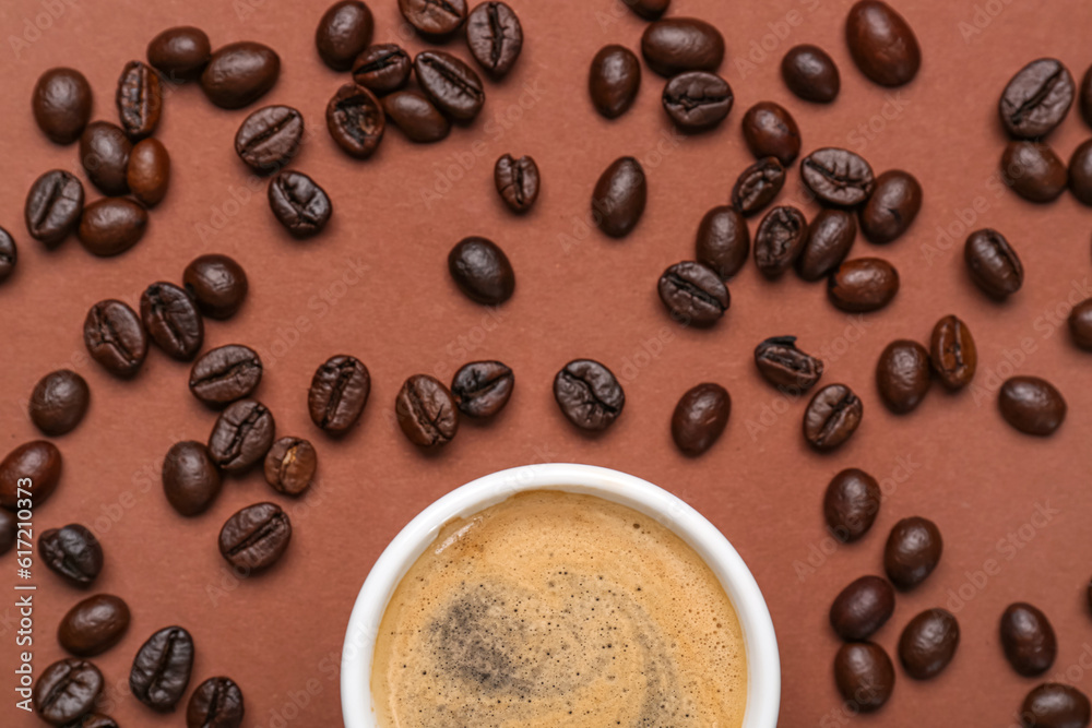 Cup of hot espresso and coffee beans on brown background