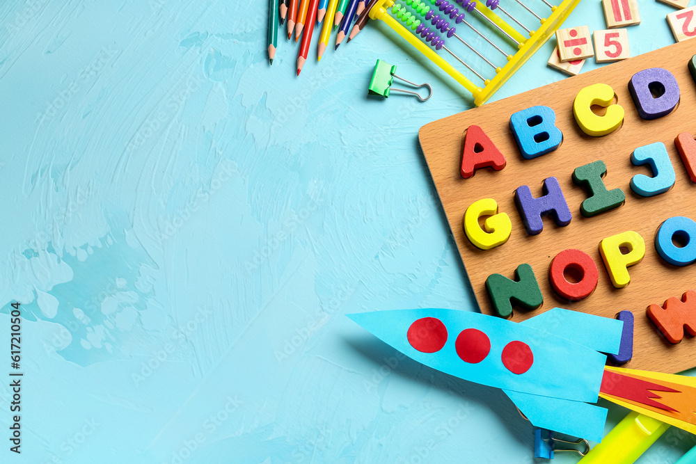 Color paper rocket with abacus, wooden letters and pencils on color background