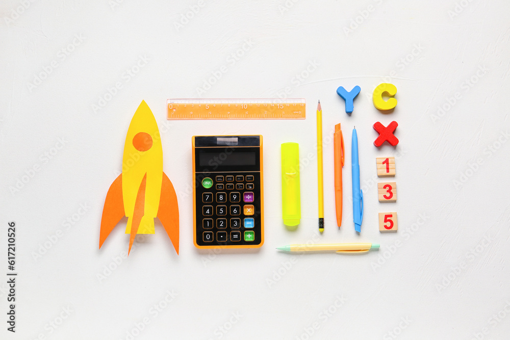 Yellow paper rocket with calculator, pens and ruler on white background