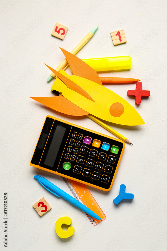 Yellow paper rocket with calculator, pens and ruler on white background