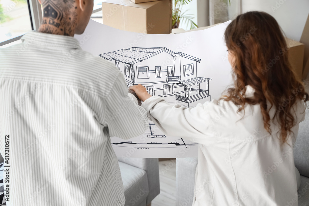 Young couple with house plan in room on moving day, back view