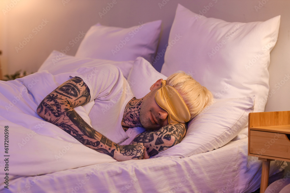 Young tattooed man sleeping in bed at night