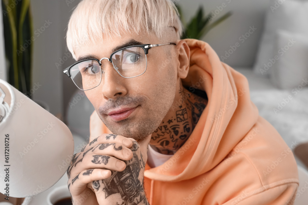 Young tattooed man in eyeglasses at home, closeup