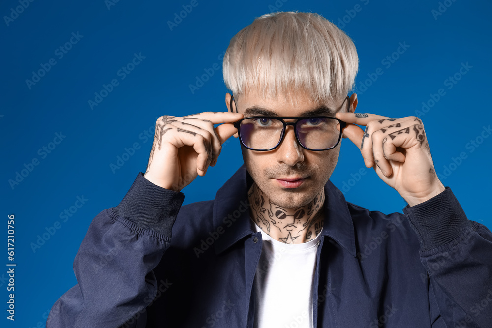 Young tattooed man in eyeglasses on blue background