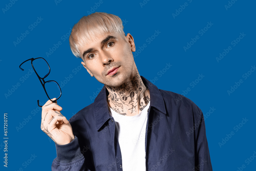 Young tattooed man with eyeglasses on blue background