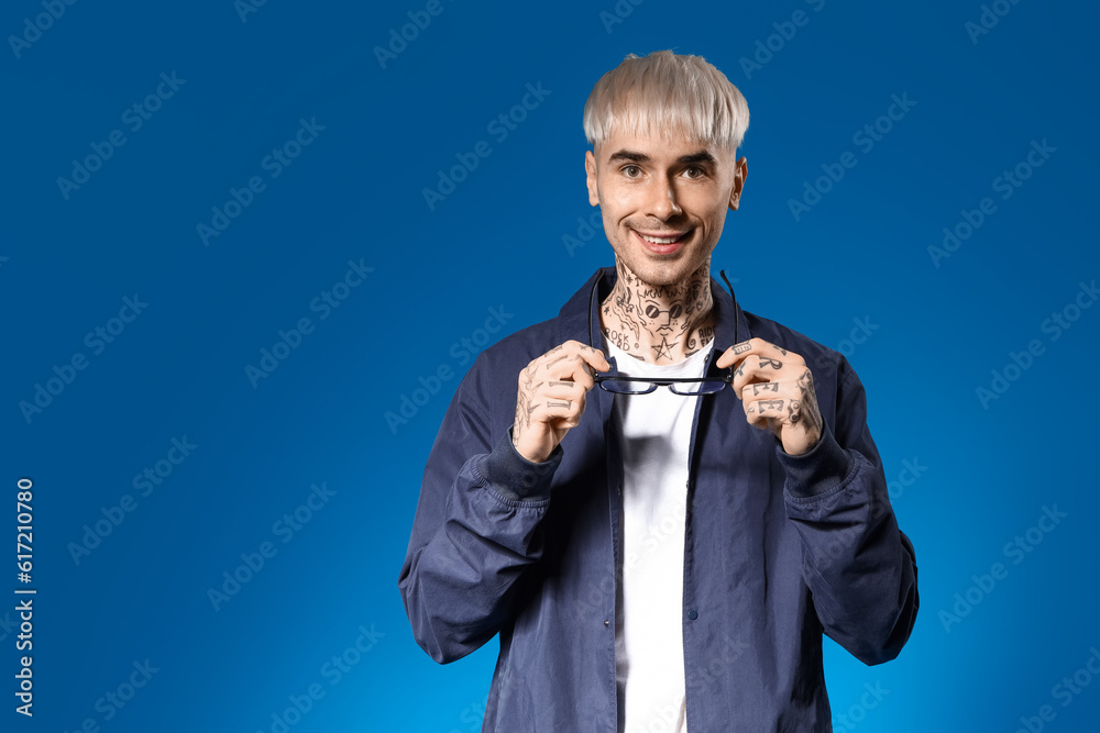 Young tattooed man with eyeglasses on blue background