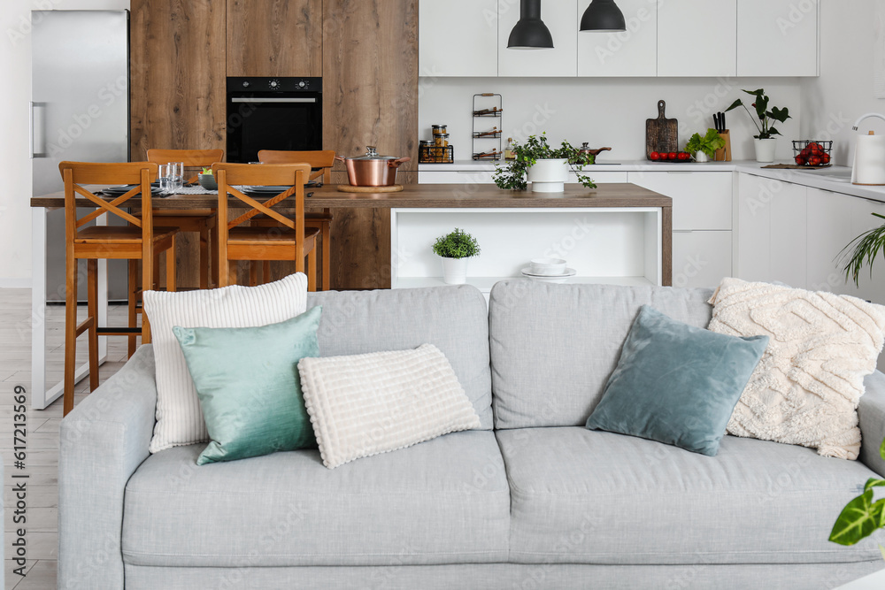 Interior of light open space kitchen with cozy grey sofa and island table