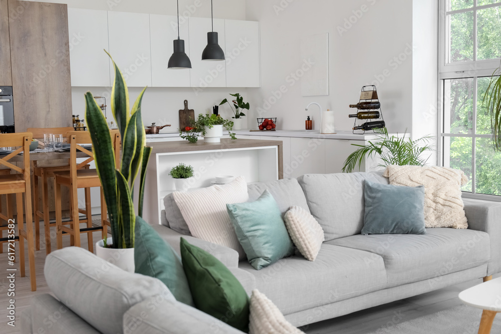 Interior of light open space kitchen with cozy grey sofas and island table