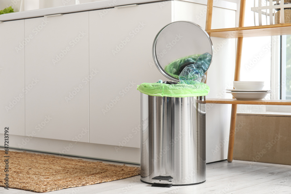 Opened trash bin with garbage in interior of light kitchen