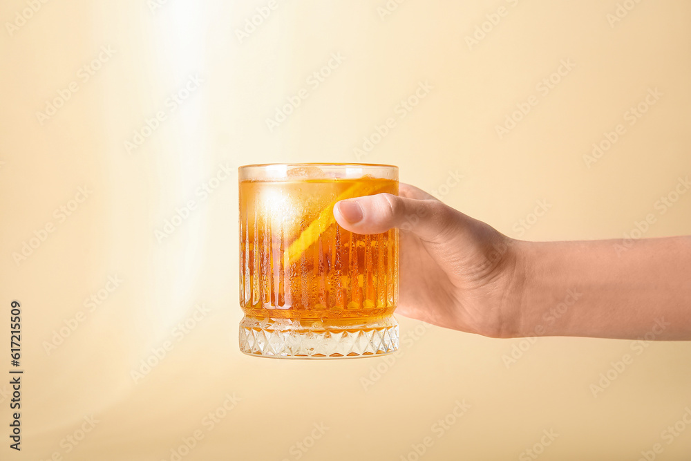 Female hand holding glass of ice tea with orange on beige background