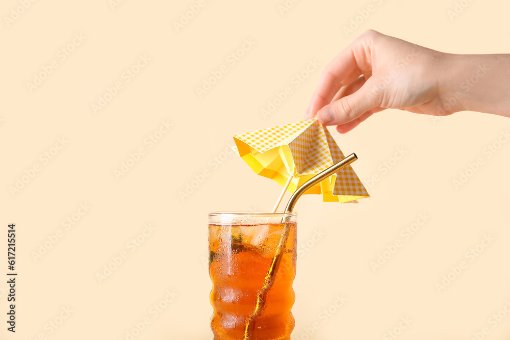 Woman decorating glass of ice tea with umbrella on beige background