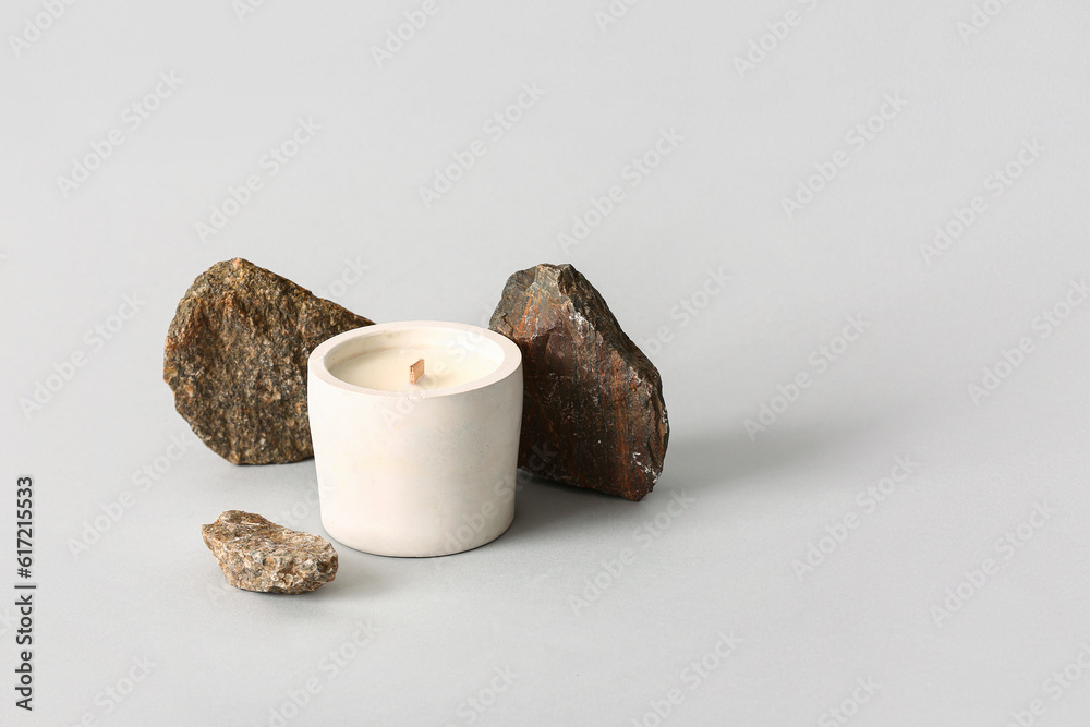 Holder with candle and stones on grey background