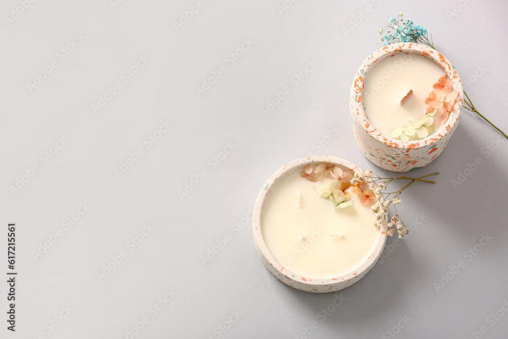 Holders with candles and flowers on grey background