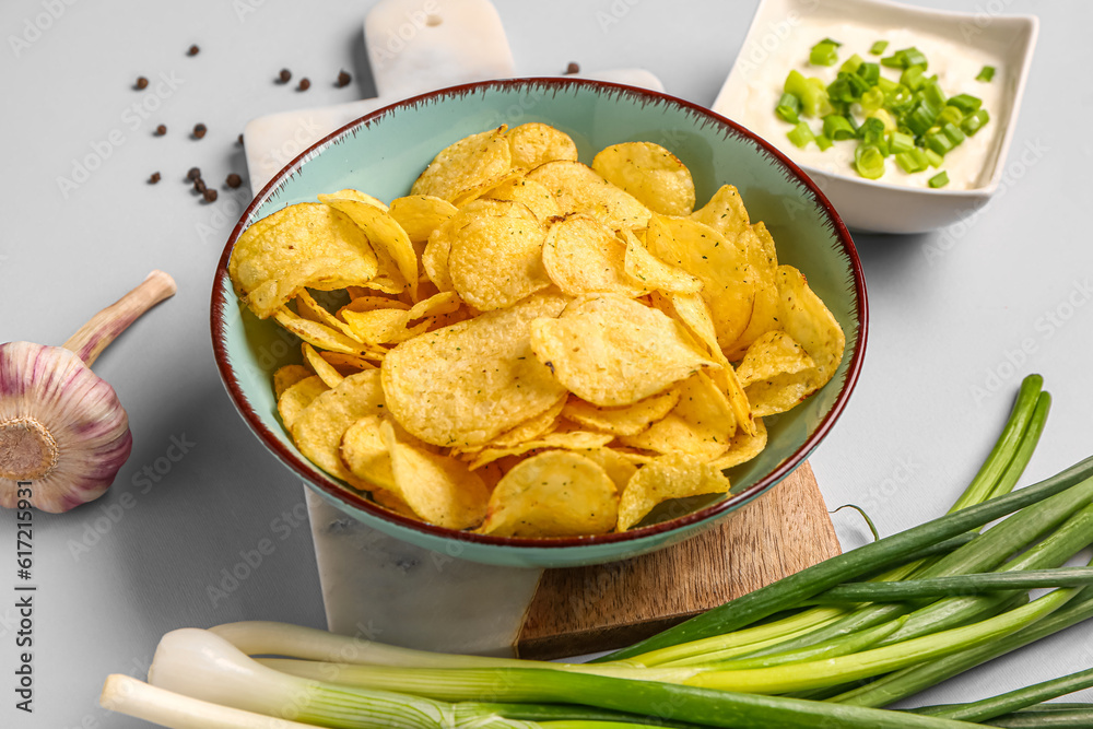 Bowl of tasty sour cream with sliced green onion and potato chips on grey background