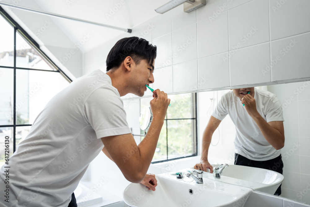 Asian young man brushing teeth and look at mirror in bathroom at home. 