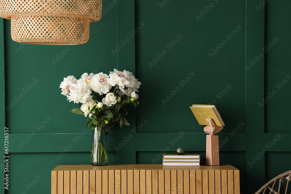 Vase of white peonies with dresser and lamp near green wall