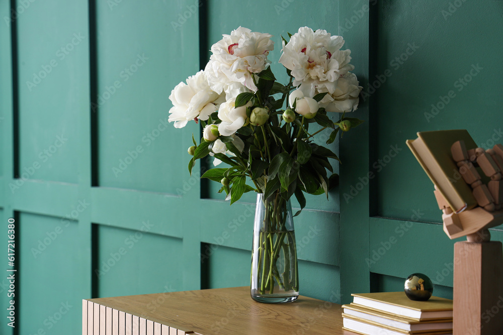 Vase of white peonies with books on dresser near green wall