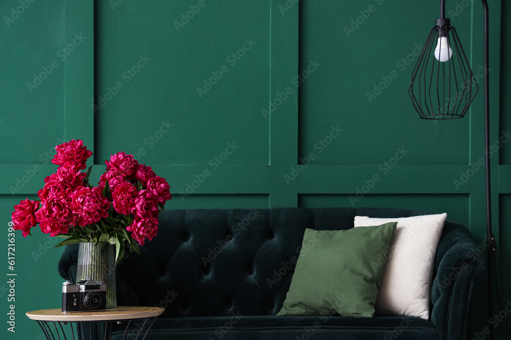 Vase of red peonies with coffee table, couch and floor lamp near green wall