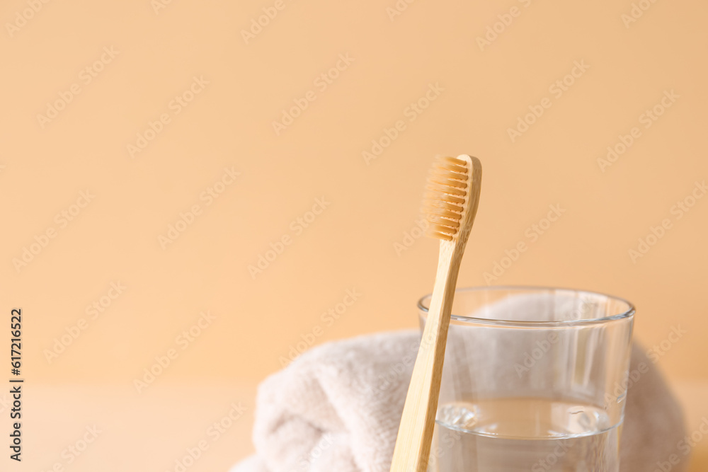 Bamboo tooth brush, glass of water and towel on beige background, closeup