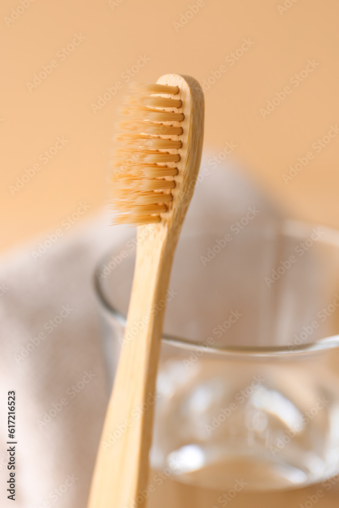 Bamboo tooth brush and glass of water on beige background, closeup