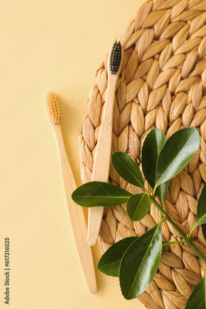 Bamboo tooth brushes and wicker mat on beige background, top view