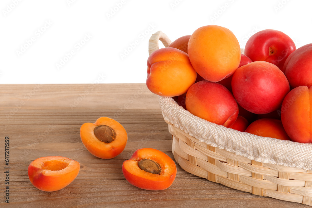 Wicker basket with ripe apricots on table against white background