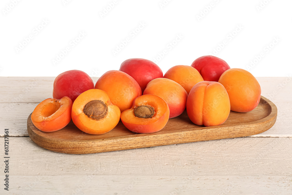 Wooden board with ripe apricots on table against white background