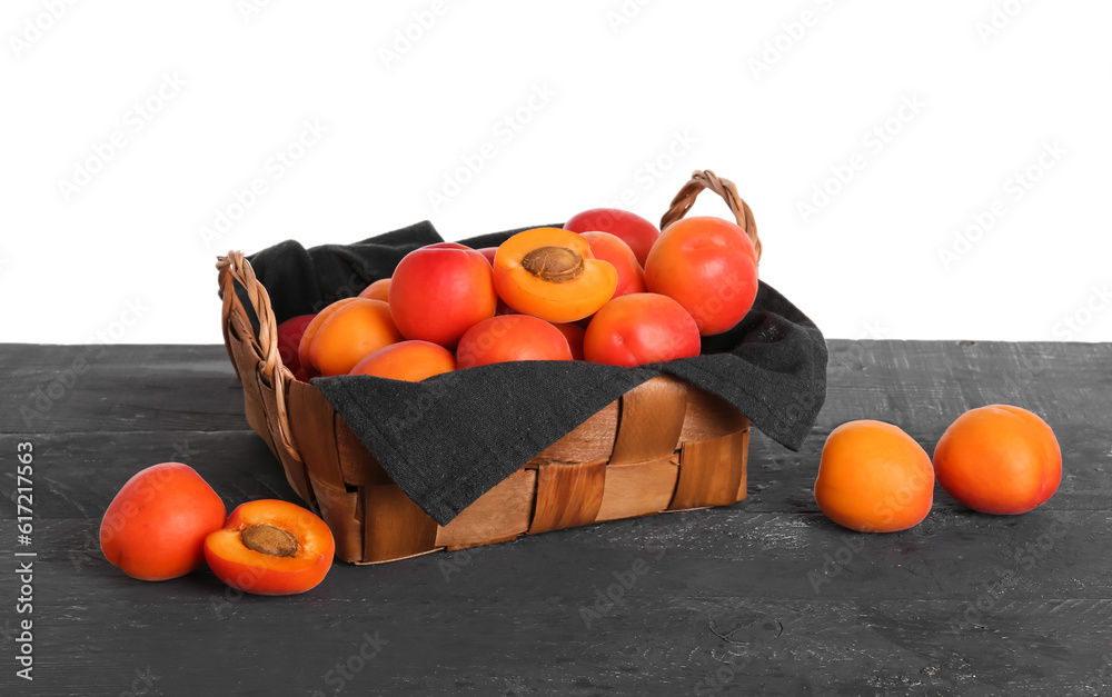 Wicker basket with ripe apricots on table against white background