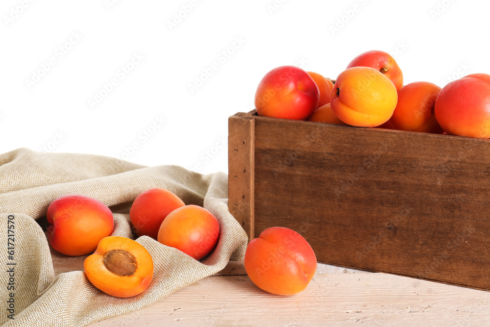 Wooden box with ripe apricots on table against white background