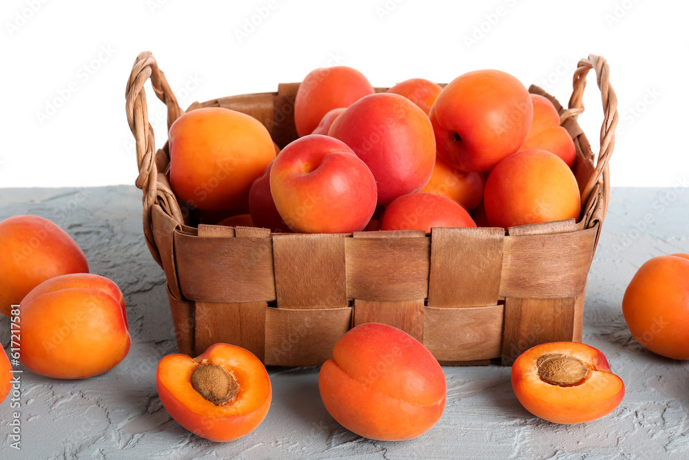 Wicker basket with ripe apricots on table against white background