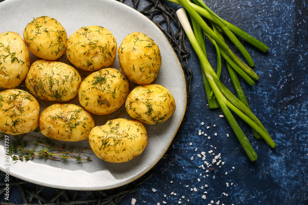 Plate of boiled baby potatoes with dill and green onion on blue background