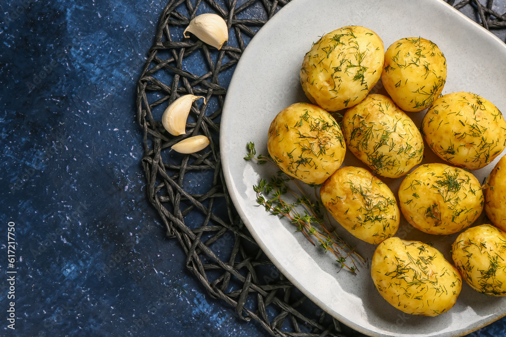 Plate of boiled baby potatoes with dill and garlic on blue background