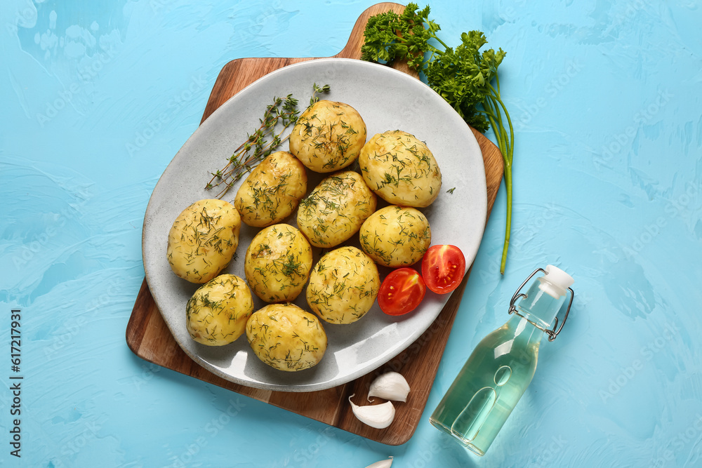 Plate of boiled baby potatoes with dill and tomatoes on blue background