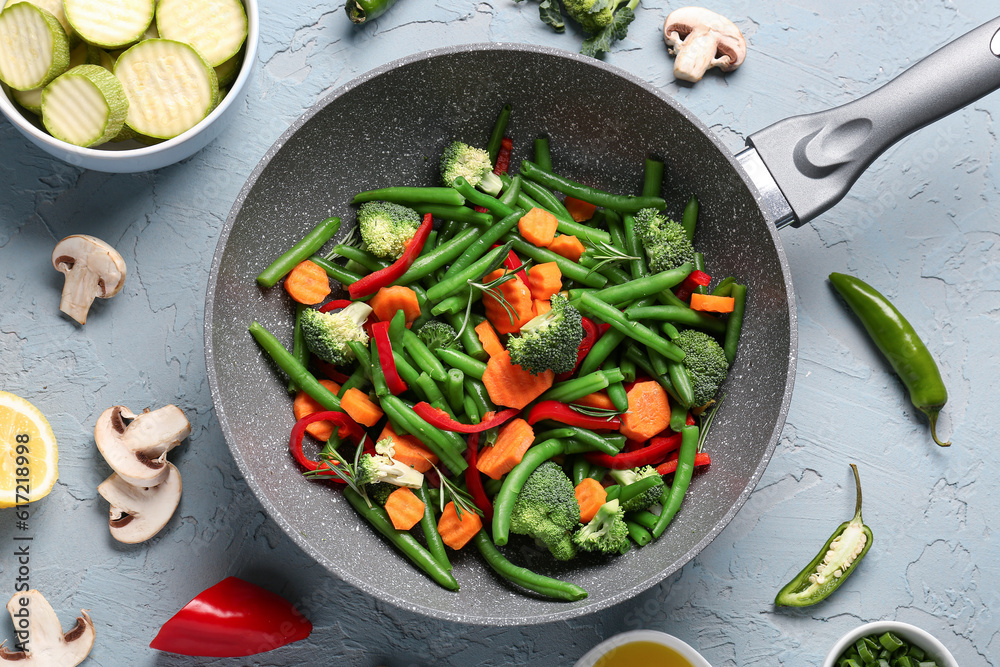 Frying pan with fresh vegetables on grey background