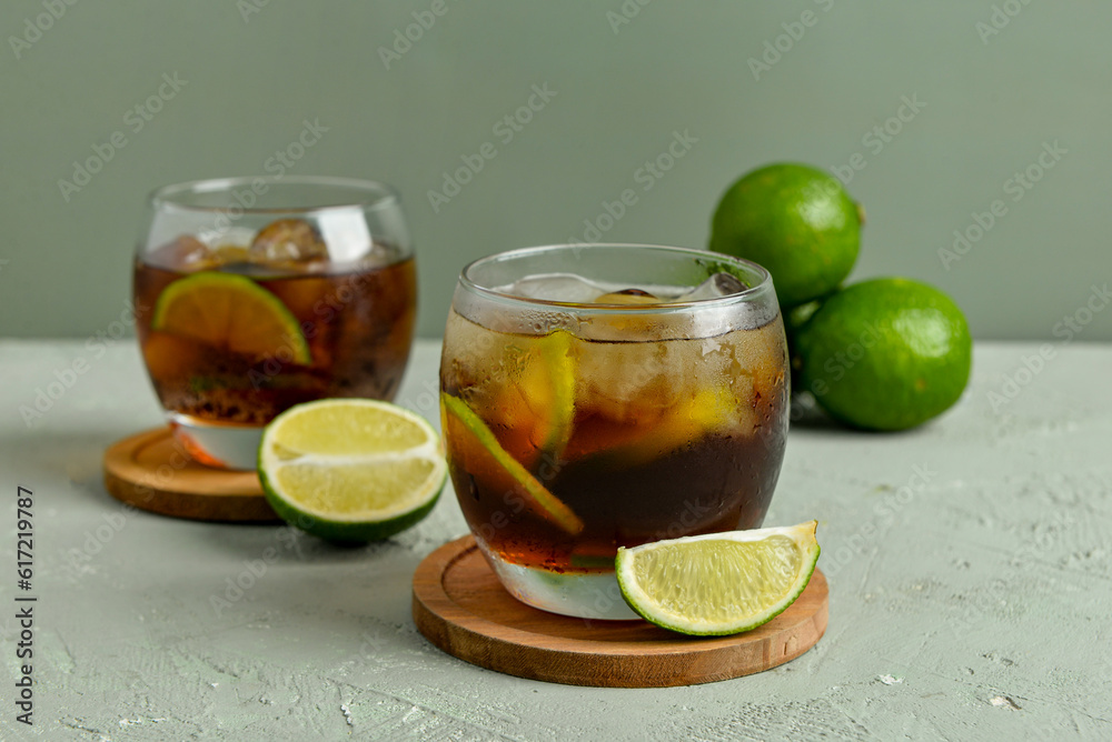 Glasses of cold Cuba Libre cocktail and limes on grey background