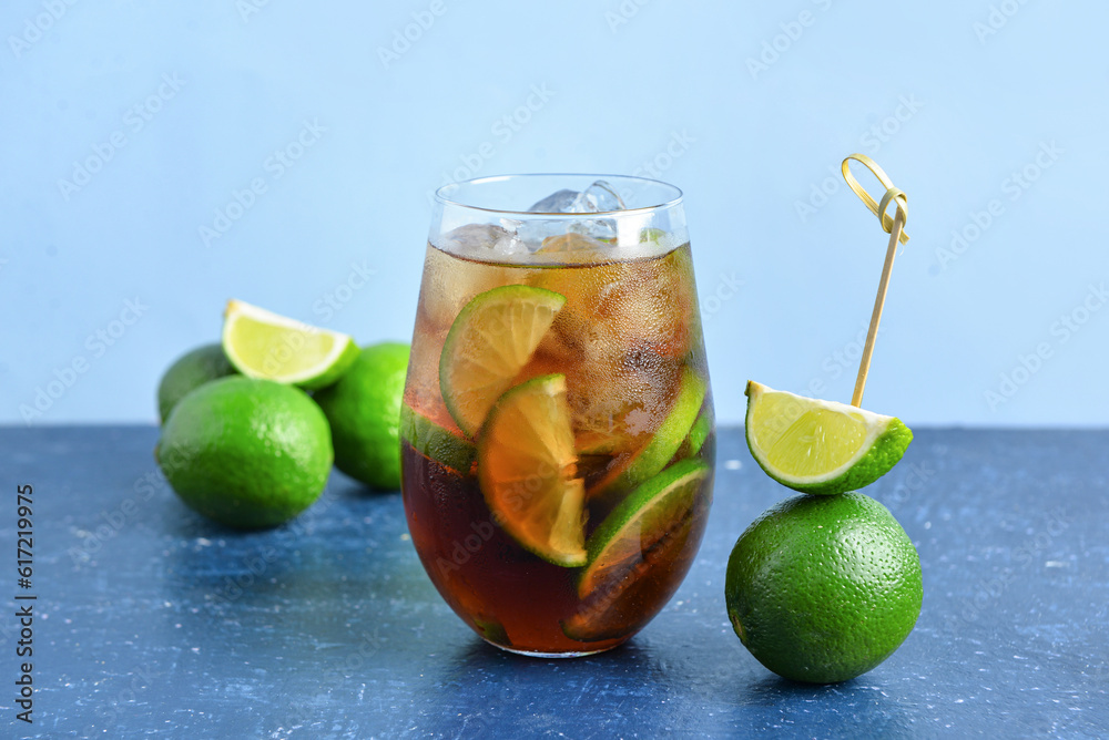 Glass of cold Cuba Libre cocktail and limes on blue table