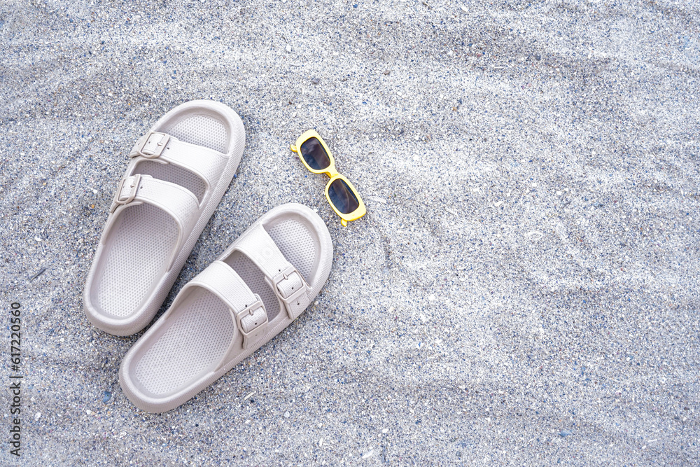 Beige flip-flops with sunglasses on sand beach background