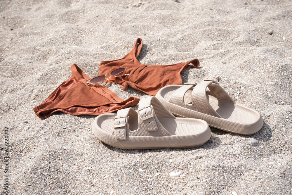 Beige flip-flops with swimsuit and sunglasses on sand beach background