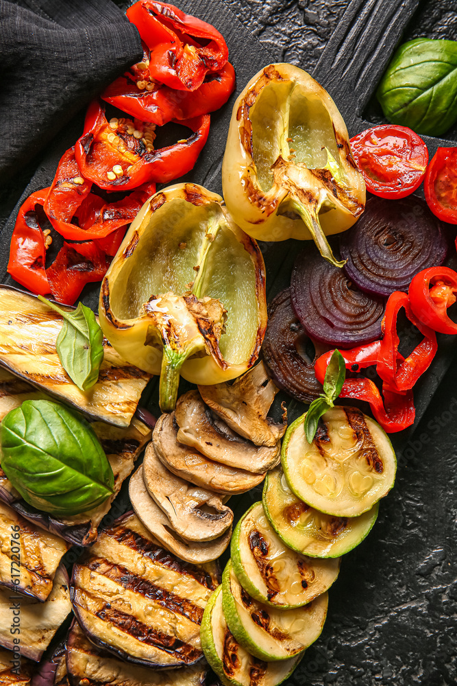 Wooden board with tasty grilled vegetables on black background