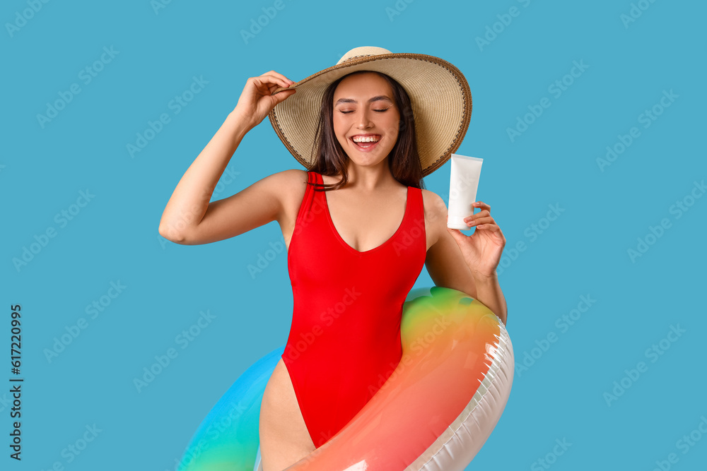 Young woman with sunscreen cream and inflatable ring on blue background