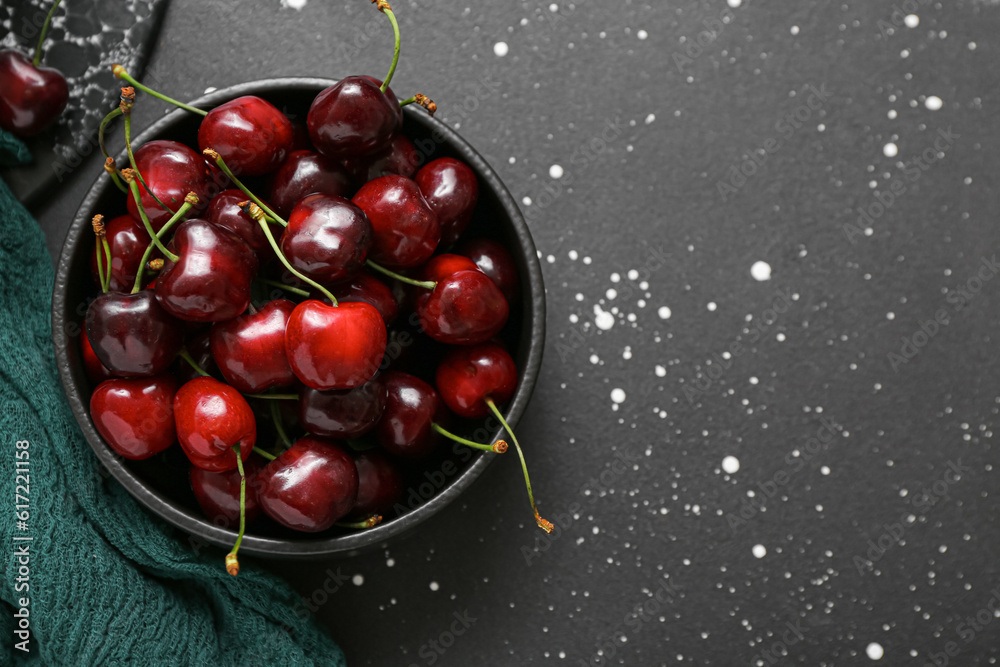 Bowl with sweet cherries on black background