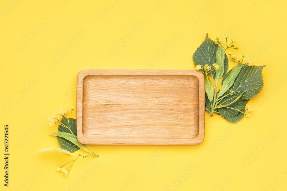 Composition with wooden board and fresh linden flowers on yellow background