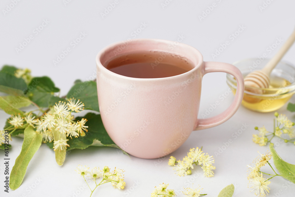 Cup of linden tea and bowl with honey on grey background