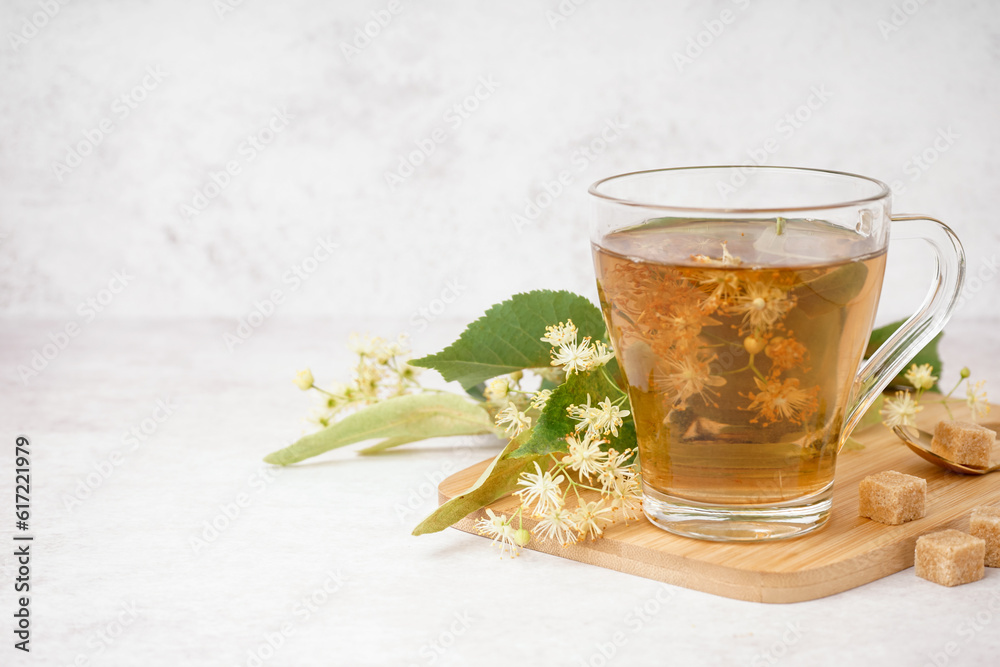 Board with glass cup of linden tea on white background